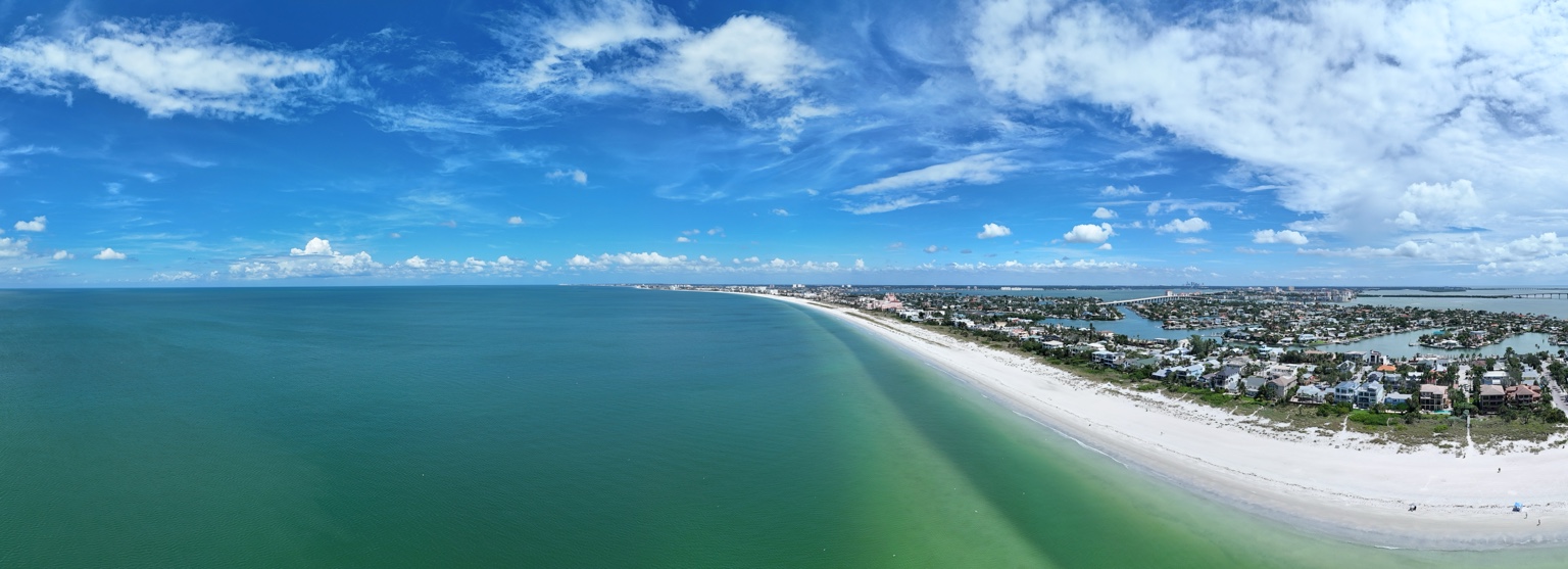 Aerial view along a white sand coastline with turquoise water, beachfront homes, and inland waterways