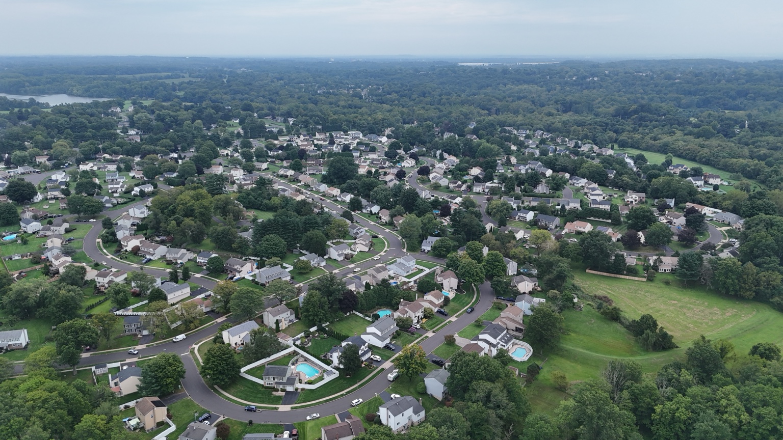 Wide aerial view across a residential neighborhood and surrounding tree line