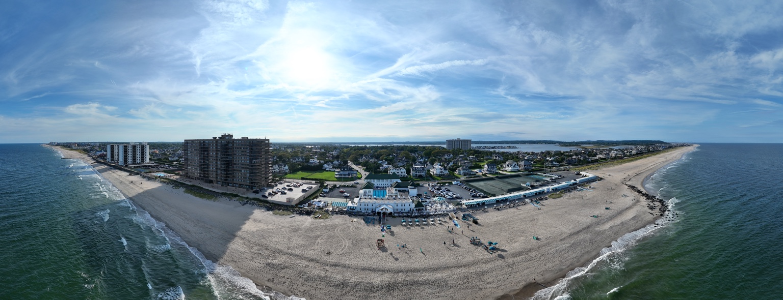 Wide coastal panorama with Monmouth Beach Bath & Tennis Club centered between sweeping views of the beach and ocean.