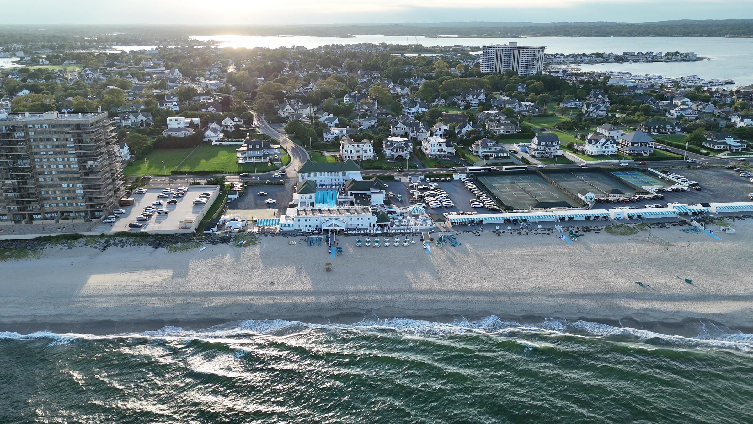 Evening aerial view of Monmouth Beach Bath & Tennis Club and the Jersey Shore, with sunlight over the water behind the venue.